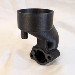 May include: A black, curved mechanical component with a cylindrical top, a small side tube, and a flanged base with two holes. The object has a textured surface and appears to be made of a rigid material.