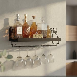 May include: A black metal wall-mounted shelf featuring a top surface holding various glass liquor bottles and a small gold sign reading BAR. Below the shelf, a rack holds five clear stemmed wine glasses, with decorative wine glass silhouettes.