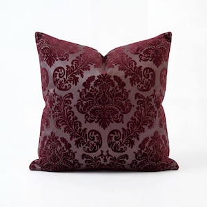 May include: A square cushion with a damask pattern. The cushion has a deep burgundy velvet pattern on a lighter grey background. The pattern is a classic, ornate design, adding a touch of elegance to home decor.