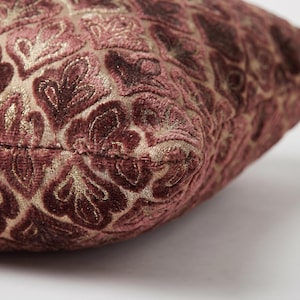 May include: A square throw pillow featuring a raised, velvet-like floral pattern in shades of deep mauve and burgundy. The fabric base is a light tan, woven material that contrasts with the soft, textured, and plush velvet floral motifs.
