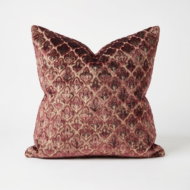 May include: A square throw pillow featuring a deep burgundy and muted pink velvet fabric with a repeating ornate floral pattern. The textured surface displays a raised, plush pile that creates a subtle contrast between the dark and light tones.