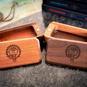 May include: Two rectangular wooden boxes with lids, one in a lighter reddish-brown wood and one in a darker brown wood. Each lid features a circular laser-engraved logo with the text "Micro World Meta Works" surrounding a central emblem.