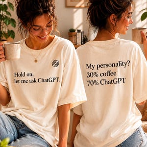 Peut inclure: Un t-shirt à col rond blanc cassé avec du texte noir et un logo. L'avant affiche le logo ChatGPT et le texte "Hold on, let me ask ChatGPT". Le dos présente le texte "My personality? 30% coffee 70% ChatGPT" imprimé en noir.