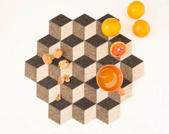 Könnte beinhalten: Ein sechseckiger Filzuntersetzer mit einem 3D-geometrischen Muster in Braun- und Beigetönen. Der Untersetzer ist mit Orangenscheiben, Walnüssen und einer kleinen orangen Tasse gefüllt mit Orangensaft verziert.
