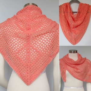 May include: A coral colored crochet shawl with a lacy openwork design. The shawl is shown draped over a mannequin.
