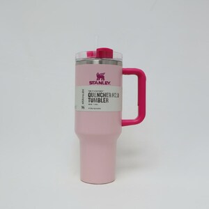 May include: A pink Stanley Quencher H2.0 Tumbler with a pink handle and lid. The tumbler has a white label with black text and a logo. It is designed to hold 40 oz (1.18 L) of liquid.