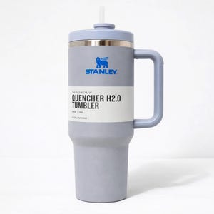 May include: A gray Stanley Quencher H2.0 Tumbler with a light blue lid, handle, and straw. The tumbler has a silver band and the Stanley logo in blue. The text "QUENCHER H2.0 TUMBLER" is printed on the front. It holds 40 oz (1.18L).