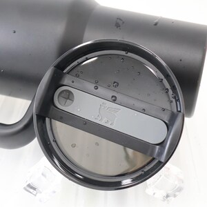 May include: A black insulated tumbler with a matching lid. The lid features a gray slider with the Stanley logo and a drinking hole. Water droplets are visible on the lid's surface. The tumbler is designed to keep beverages cold or hot.
