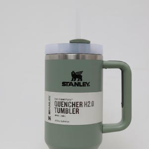 May include: A green Stanley Quencher H2.0 Tumbler with a white straw and a handle. The tumbler has a white band with the text "QUENCHER H2.0 TUMBLER" and "40 OZ | 1.18 L". The lid is light blue.