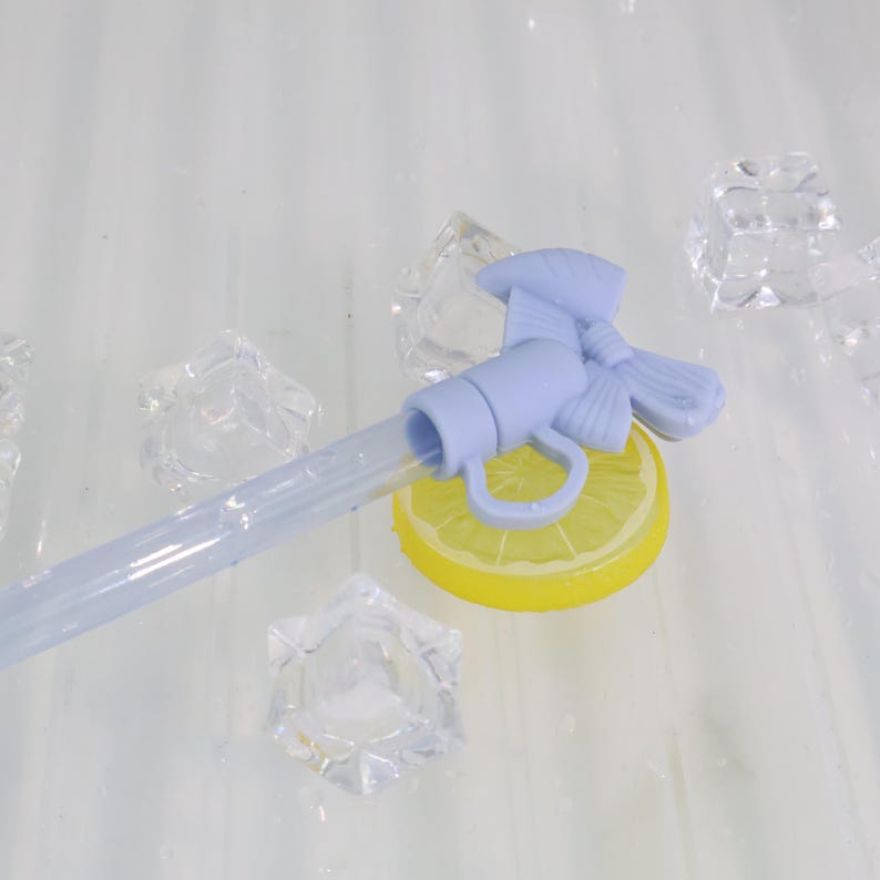 K&ouml;nnte beinhalten: Ein hellblauer Getr&auml;nkespenderhahn mit Schleifendetail, der auf einer gelben Zitronenscheibe ruht. Ein klarer Schlauch erstreckt sich vom Wasserhahn. Klare Eisw&uuml;rfel sind um den Wasserhahn und die Zitronenscheibe verstreut.