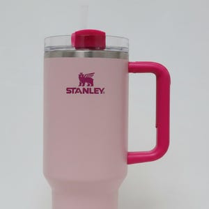 May include: A pink Stanley tumbler with a magenta handle, lid, and logo. The tumbler has a clear plastic lid and a reusable straw. The Stanley logo is printed in magenta on the front of the tumbler.
