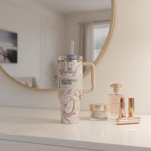 K&ouml;nnte beinhalten: Ein gro&szlig;er, isolierter Becher mit Griff und Strohhalm, mit einem Wirbelmuster aus Wei&szlig;, Beige und Braun. Der Becher tr&auml;gt den Text "QUENCHER H2.0 TUMBLER". Daneben befinden sich Sch&ouml;nheitsprodukte, darunter Lippenstifte und Parf&uuml;m.