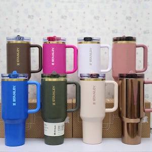 Puede incluir: Una colecci&oacute;n de tazas Stanley aisladas en varios colores, incluyendo marr&oacute;n, rosa, blanco, azul, verde y beige. Cada taza tiene un asa, una tapa y el logotipo de Stanley. Las tazas est&aacute;n dise&ntilde;adas para bebidas fr&iacute;as y calientes.