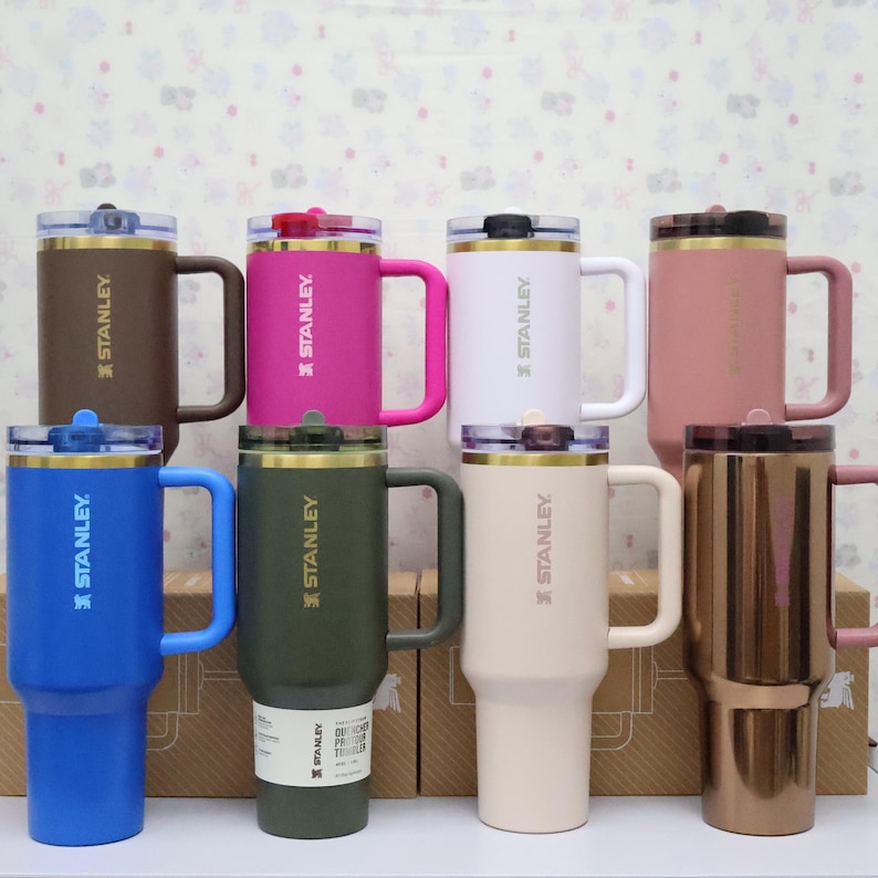 Puede incluir: Una colecci&oacute;n de tazas Stanley aisladas en varios colores, incluyendo marr&oacute;n, rosa, blanco, azul, verde y beige. Cada taza tiene un asa, una tapa y el logotipo de Stanley. Las tazas est&aacute;n dise&ntilde;adas para bebidas fr&iacute;as y calientes.