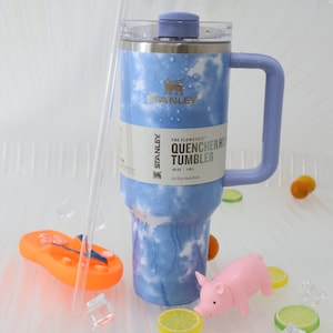 K&ouml;nnte beinhalten: Ein Stanley Flowstate Quencher H2.0 Becher mit blau-wei&szlig;em Wolkenmuster. Der Becher hat einen Griff und einen Deckel. Der Text auf dem Becher lautet "40 oz | 1,18 L All Day Hydration".