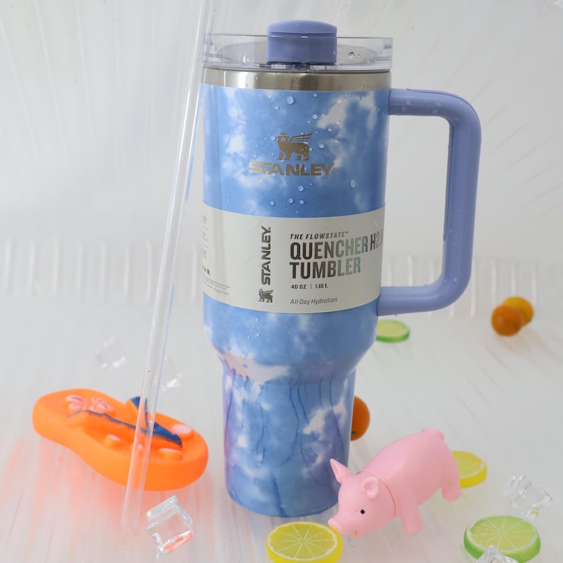 K&ouml;nnte beinhalten: Ein Stanley Flowstate Quencher H2.0 Becher mit blau-wei&szlig;em Wolkenmuster. Der Becher hat einen Griff und einen Deckel. Der Text auf dem Becher lautet "40 oz | 1,18 L All Day Hydration".