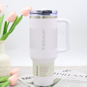 Puede incluir: Vaso Stanley Quencher Protour blanco con asa y tapa transparente. El vaso tiene el logotipo de Stanley y texto en el lateral. Dise&ntilde;ado para la hidrataci&oacute;n durante todo el d&iacute;a.