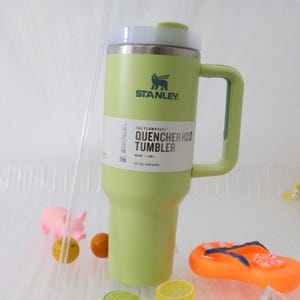 Puede incluir: Un vaso Stanley Quencher H2.0 verde claro con tapa y asa blancas. El vaso tiene el logotipo de Stanley y la informaci&oacute;n del producto impresa en el lateral. Tiene una capacidad de 1,18 L y est&aacute; dise&ntilde;ado para la hidrataci&oacute;n durante todo el d&iacute;a.