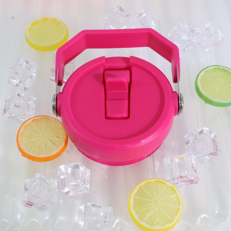 May include: A bright pink water bottle lid with a handle and a flip-top closure. The lid is surrounded by ice cubes and slices of lemon and orange. The lid is made of plastic and has a smooth surface.