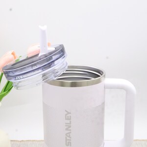 Puede incluir: Taza Stanley blanca con asa y tapa transparente con pajita blanca. La taza tiene un borde plateado y el logotipo de Stanley impreso en el lateral. Para bebidas fr&iacute;as o calientes.