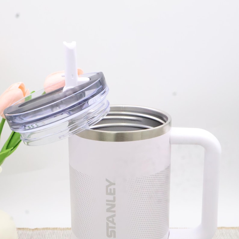 Puede incluir: Taza Stanley blanca con asa y tapa transparente con pajita blanca. La taza tiene un borde plateado y el logotipo de Stanley impreso en el lateral. Para bebidas fr&iacute;as o calientes.