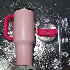 May include: A pink insulated tumbler with a bright pink handle and lid accents. The tumbler has a stainless steel rim and a clear lid with a pink slider. A clear straw is included. Ice cubes and water droplets are scattered around the tumbler.