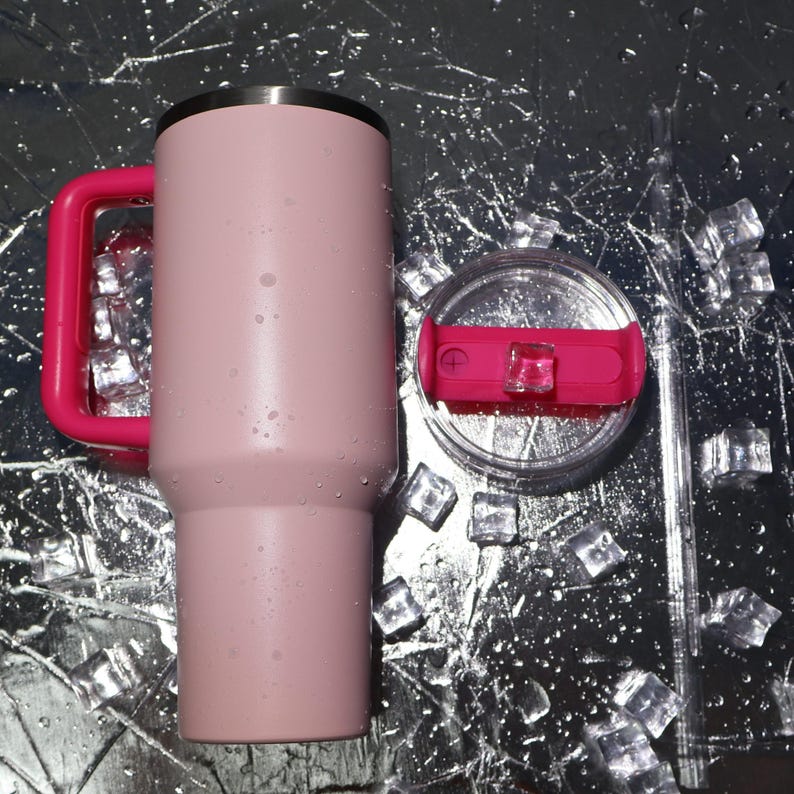 May include: A pink insulated tumbler with a bright pink handle and lid accents. The tumbler has a stainless steel rim and a clear lid with a pink slider. A clear straw is included. Ice cubes and water droplets are scattered around the tumbler.