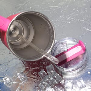 Peut inclure: Un gobelet isotherme rose et argent&eacute; avec une paille et un couvercle transparents. Le couvercle est partiellement ouvert et des gla&ccedil;ons sont &eacute;parpill&eacute;s autour de la base. Le gobelet est con&ccedil;u pour garder les boissons froides.