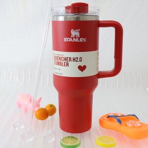 Puede incluir: Un vaso Stanley Quencher H2.0 rojo con asa, tapa transparente y pajita. El vaso tiene el logotipo de Stanley y las palabras "QUENCHER H2.0 TUMBLER" impresas. El vaso es de 1,18 L.