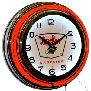 May include: A round, illuminated wall clock with a black and orange neon ring. The clock face is white with black numerals and hands. The Sinclair logo, featuring a green dinosaur, is prominently displayed.