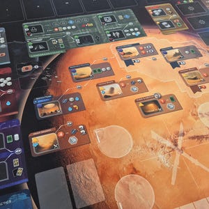 May include: A board game with a Martian theme. The game board is predominantly orange and brown, depicting a map of Mars. Various game pieces, cards, and player boards are arranged on the board. The game components feature detailed illustrations and text, enhancing the strategic gameplay.
