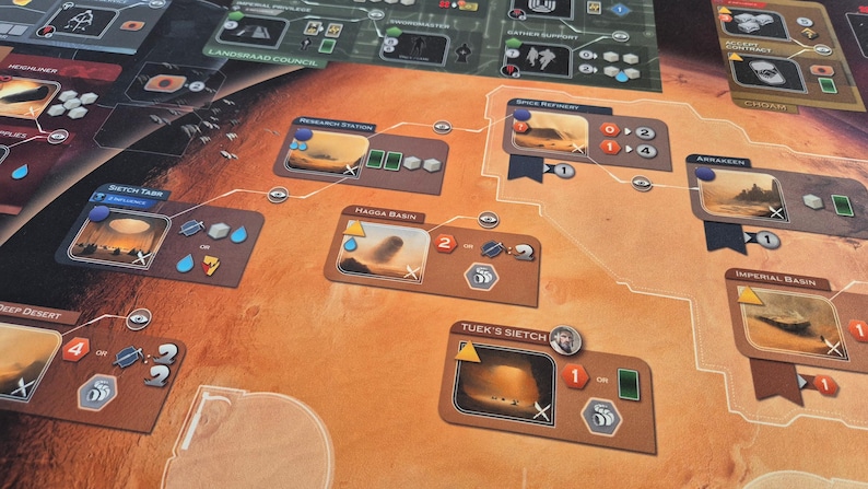 May include: A board game with a Martian landscape theme. The game board features various locations with illustrations and icons. Cards and tokens are scattered across the board, with a color palette of brown, orange, and green.