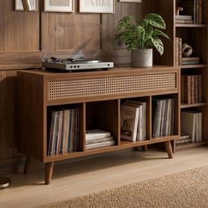 May include: A mid-century modern style record player console in a warm brown finish. The console features a woven rattan front panel, open storage compartments for records and books, and a silver turntable on top.
