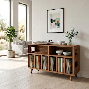Puede incluir: Consola de tocadiscos de madera de estilo moderno de mediados de siglo, con un tocadiscos en la parte superior y almacenamiento de discos debajo. La consola marrón tiene patas en ángulo. Hay una impresión artística abstracta enmarcada en la pared.