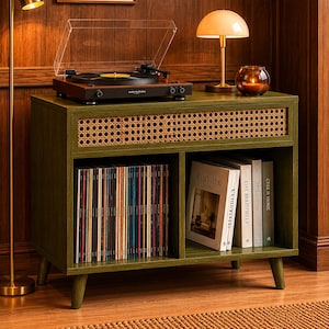 May include: A green record player console with a woven front panel and angled legs. The console holds a turntable, vinyl records, and books. A gold lamp and a candle holder sit on top. The turntable is dark brown.
