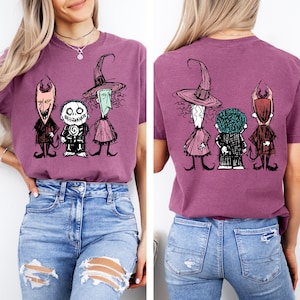 May include: A mauve short-sleeved t-shirt featuring a graphic print of three cartoon characters. The front displays the characters facing forward, while the back shows the same three characters from behind, all rendered in a sketch-like black ink style.
