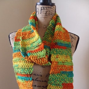 May include: A handmade crochet scarf in a vibrant mix of colors, including orange, yellow, green, and teal. The scarf is displayed on a mannequin, showcasing its textured, striped pattern. This accessory is perfect for adding a pop of color to any outfit.