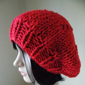 May include: A vibrant red knit beret. The hat is made of thick, textured yarn, with a classic beret shape. The beret is worn on a mannequin head with black hair.