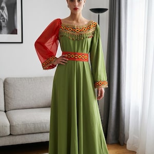 Könnte beinhalten: Ein bodenlanges olivgrünes Kleid mit einem roten, transparenten Puffärmel auf der rechten Seite und einem langen grünen Ärmel auf der linken Seite. Das Kleid hat einen roten Taillengürtel und einen Ausschnitt mit roter, gelber und schwarzer Stickerei.