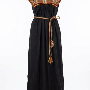 K&ouml;nnte beinhalten: Ein bodenlanges schwarzes Kleid mit quadratischem Ausschnitt und kurzen &Auml;rmeln, verziert mit mehrfarbigen Stickb&auml;ndern in Blau-, Gelb- und Rott&ouml;nen. Das Kleid verf&uuml;gt &uuml;ber ein passendes geflochtenes Taillenband mit Quastenenden.