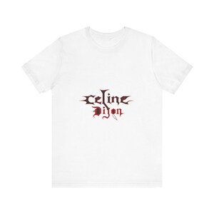 Peut inclure: Un t-shirt blanc avec l'inscription "Celine Dijon" en rouge foncé. Le texte est écrit dans une police de style gothique et est centré sur le devant du t-shirt. Le design est simple mais percutant.