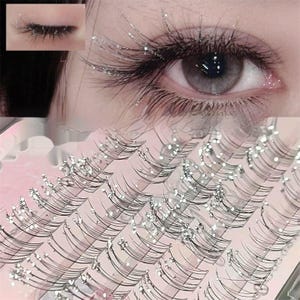 May include: Close-up of an eye with long, black eyelashes and silver glitter accents. A set of false eyelashes is displayed below. The eye is gray with a hint of pink. The image includes a smaller inset of the eye with eyelashes.