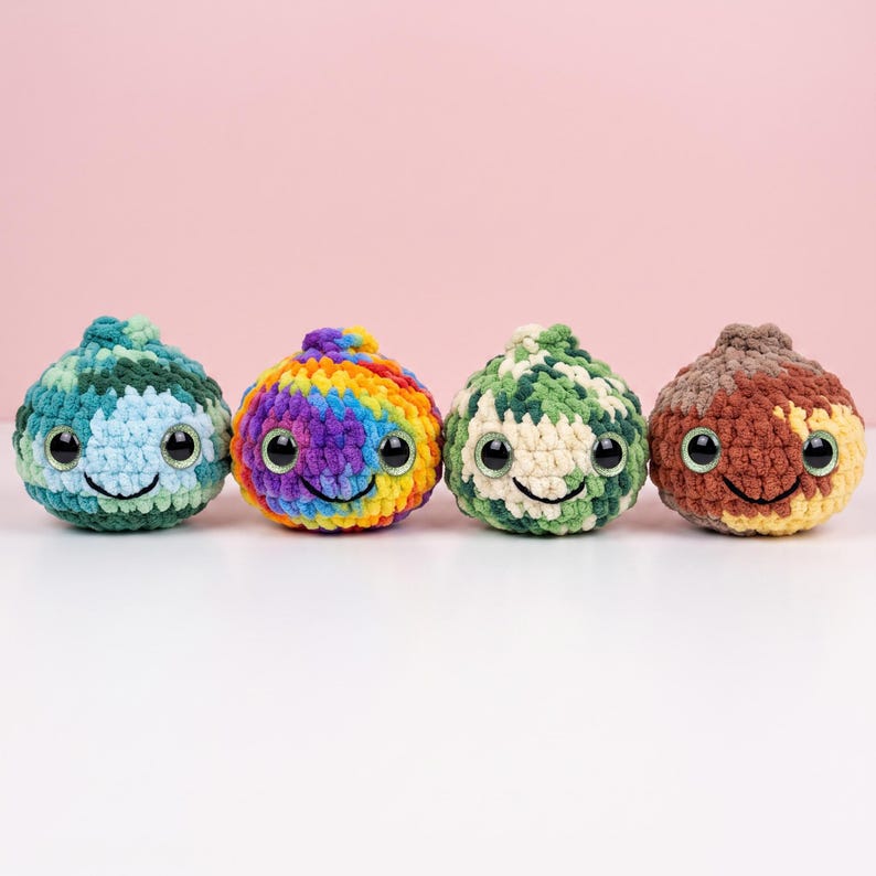 May include: Four round, crocheted plush toys arranged in a row. Each features a textured yarn surface, large black plastic safety eyes with green irises, and a stitched black smile. The colors include blue-green, rainbow, green-white, and brown-tan.