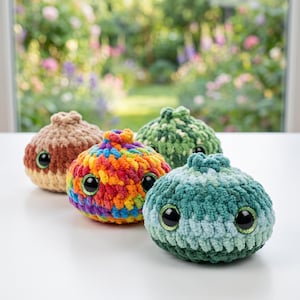 May include: Four round, plush, crocheted creatures with large, glossy black eyes. One is multicolored with bright rainbow yarn, one is solid tan, one is dark green, and one is a variegated teal and light blue. Each has a small top knot.