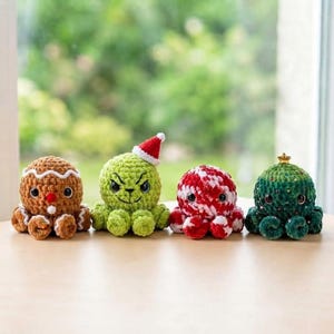 K&ouml;nnte beinhalten: Vier geh&auml;kelte Pl&uuml;schtiere in einer Reihe. Das erste ist ein brauner Lebkuchenmann, das zweite ein gr&uuml;nes Wesen mit einer rot-wei&szlig;en Weihnachtsmannm&uuml;tze, das dritte ein rot-wei&szlig; gestreifter Ball und das vierte ein gr&uuml;ner Weihnachtsbaum.