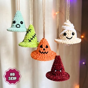 Op de afbeelding: Vijf kegelvormige gehaakte ornamenten hangend aan touwtjes. De set bevat een lichtblauw spookje, een limoengroen monster met stiksels, een oranje pompoen, een witte mummie en een donkerrode vampier. Een roze badge toont de tekst NO SEW.