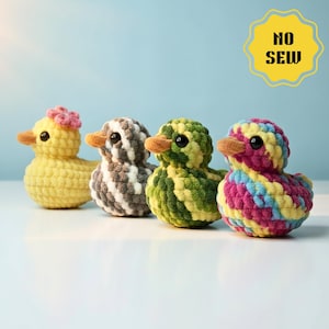 Könnte beinhalten: Vier handgefertigte Häkelenten in einer Reihe. Die Enten sind gelb, grau und weiß, grün und gelb sowie rosa, gelb und blau. Jede Ente hat einen orangefarbenen Schnabel und schwarze Augen. Die gelbe Ente hat eine rosa Blume. Der Text "NO SEW" ist enthalten.