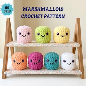 May include: A wooden shelf displays seven colourful, crocheted marshmallow-shaped toys. Each marshmallow has a smiling face with black stitched mouths and purple eyes. The text "MARSHMALLOW CROCHET PATTERN" is above the toys.