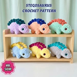 May include: Six plush Stegosaurus toys made with crochet yarn, displayed on a two-tier wooden shelf. The text STEGOSAURUS CROCHET PATTERN and NO SEW are visible. The dinosaurs are purple, peach, mint green, light blue, yellow, and gray.