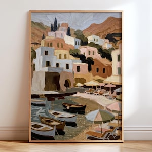 May include: A framed vertical wall art print depicting a coastal village scene with stacked buildings in shades of beige, tan, and blue. Several small boats float in the water near a sandy beach with umbrellas and lounge chairs.